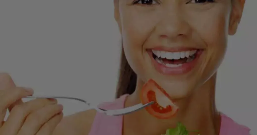 A smiling Girl holds a fork with a piece of salad, showcasing her enjoyment of a healthy meal